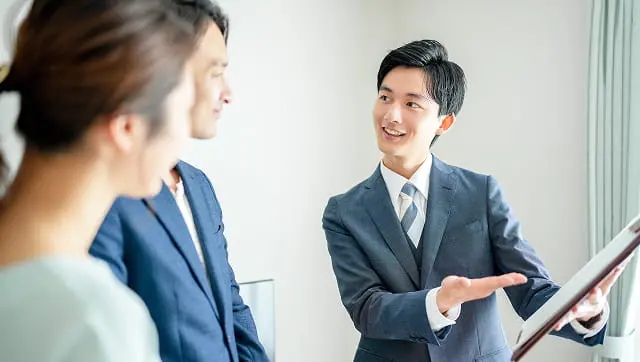 明るい室内で男性が資料を見せながら説明しているシーン